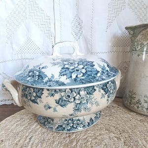 Puede incluir: Una taza de cerámica blanca con un asa negra y el texto "But First, Coffee" en un estilo manuscrito. La taza está sobre una superficie blanca. La taza mide aproximadamente 10 cm de alto.