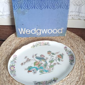 Peut inclure: Un plat de service ovale en céramique blanche avec un bord doré, orné d'un paon coloré et d'un motif floral. Le plat est présenté avec sa boîte bleue d'origine, sur laquelle est imprimé le mot "Wedgwood".