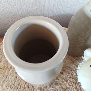 May include: A cylindrical ceramic vessel with a smooth, off-white glazed finish and a wide, rounded rim. The interior is hollow and deep, showing a consistent light-coloured surface. The object is positioned upright, revealing its circular opening.