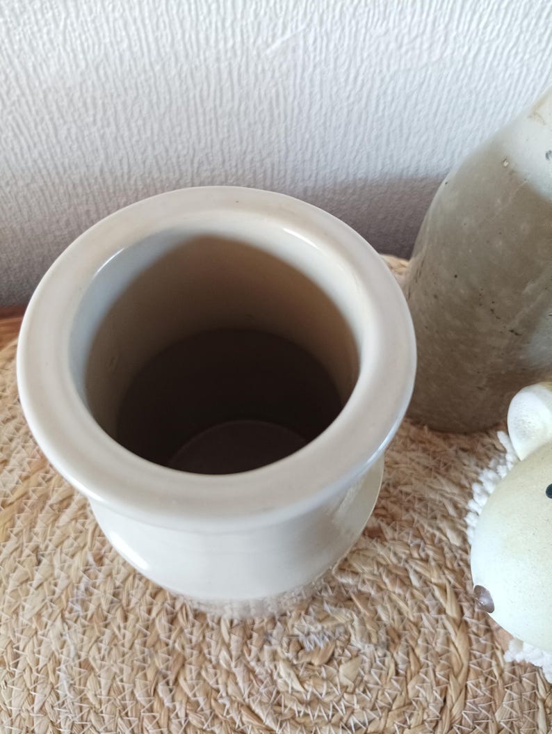May include: A cylindrical ceramic vessel with a smooth, off-white glazed finish and a wide, rounded rim. The interior is hollow and deep, showing a consistent light-coloured surface. The object is positioned upright, revealing its circular opening.