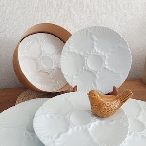 Puede incluir: Platos de ostras de cerámica blanca con seis compartimentos, exhibidos con una figura de pájaro de cerámica marrón. Los platos tienen un diseño festoneado. Un plato está dentro de un recipiente redondo marrón.