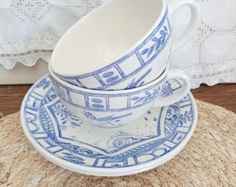 May include: A white ceramic teacup and saucer set featuring a blue transferware pattern. The cup and saucer are decorated with detailed illustrations of birds, foliage, and geometric borders in a classic blue and white colour scheme.
