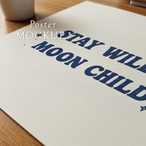 May include: A poster mockup with the words "STAY WILD MOON CHILD" in dark blue, stylized font. The poster is on a textured, off-white surface, with a small star graphic. The words "Poster Mockup" are in white text.