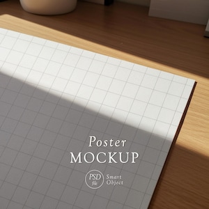 May include: A white poster mockup with a grid pattern, angled on a wooden surface. The text "Poster MOCKUP" is displayed, along with "PSD file" and "Smart Object" text. The scene is lit with natural light.