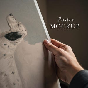 May include: A close-up of a poster mockup featuring a black and white illustration of a dog's head looking up. The poster is being held by a hand, with the text "Poster MOCKUP" visible in the upper right corner.