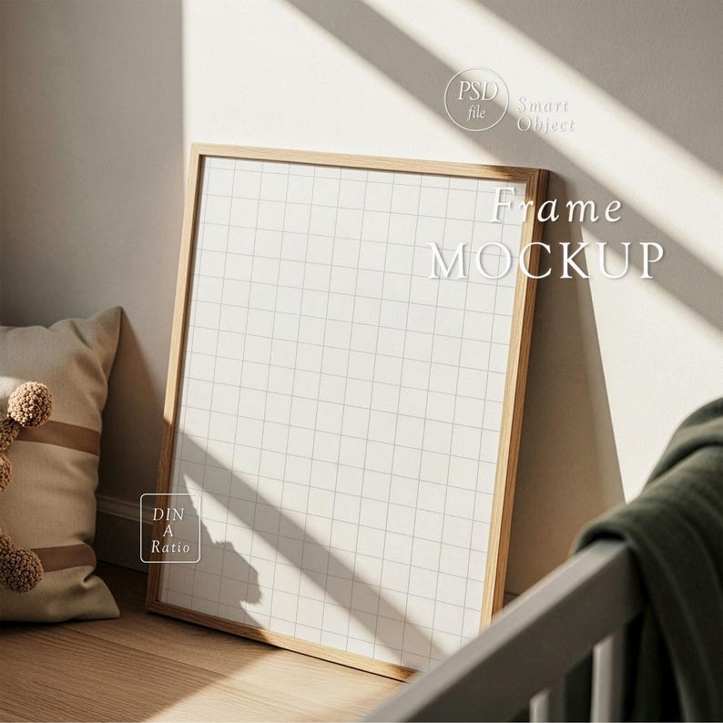Op de afbeelding: Een houten frame-mockup die tegen een muur leunt. Het frame bevat een wit papier met een rasterpatroon. De woorden "Frame MOCKUP" staan op het papier. Een kussen en een deken zijn zichtbaar op de achtergrond. De afbeelding wordt verlicht door natuurlijk licht.