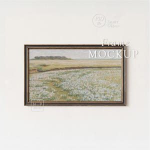 May include: A framed landscape painting featuring a field of white flowers under a cloudy sky. The artwork is in a dark wooden frame and is labeled "Frame MOCKUP" with a 16:9 ratio indicator. The overall aesthetic is vintage and serene.