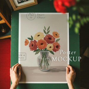 K&ouml;nnte beinhalten: Ein Poster-Mockup mit einem Gem&auml;lde eines Strau&szlig;es aus orangefarbenen, gelben und roten Blumen in einer durchsichtigen Glasvase. Das Poster liegt auf einer gr&uuml;nen Oberfl&auml;che und der Text "Poster MOCKUP" ist unten sichtbar.