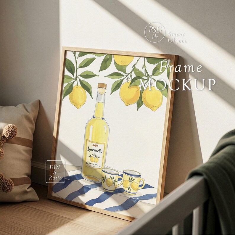 Op de afbeelding: Een ingelijste kunstdruk met een illustratie van citroenen, takken en een fles limoncello. Twee kleine mokken met citroenmotieven staan voor de fles. De lijst is van licht hout en het kunstwerk ligt op een blauw-wit gestreept oppervlak.