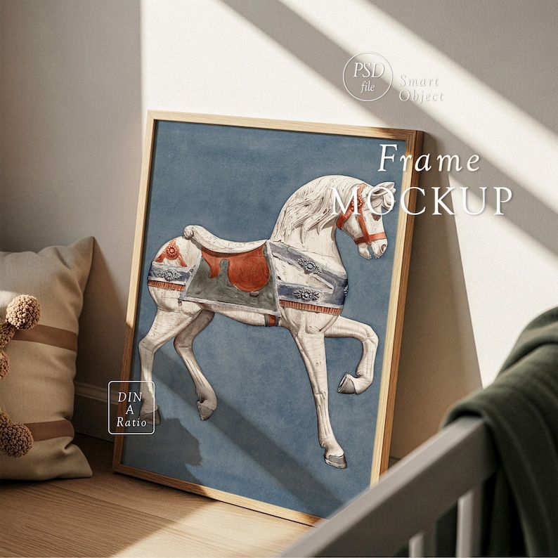Op de afbeelding: Een ingelijste print met een wit carrouselpaard met een rood zadel en blauwe accenten op een blauwe achtergrond. Het houten frame leunt tegen een muur. De tekst "Frame MOCKUP" is zichtbaar.