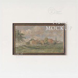 May include: A framed landscape painting with a dark wooden frame. The artwork depicts a village scene with red-roofed buildings, a church steeple, and a cloudy sky. The words "Frame MOCKUP" are displayed on the image.