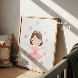 Op de afbeelding: Een ingelijste print met een cartoon ballerina in een roze jurk en kroon, omringd door roze bloemen. Het frame is van licht hout en de print leunt tegen een muur. De tekst "Frame MOCKUP" is zichtbaar.