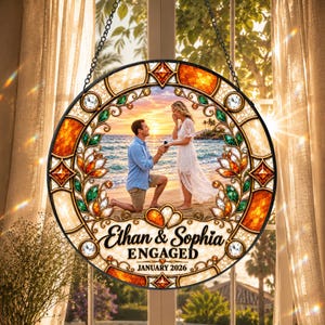 May include: A circular stained glass suncatcher featuring a central photograph of a couple on a beach during a proposal. The border displays orange and green floral patterns with clear crystals. Text reads: Ethan & Sophia ENGAGED JANUARY 2026.