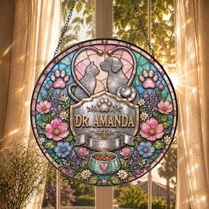 May include: A circular stained glass suncatcher featuring a cat and dog silhouette framed by a stethoscope, pink and blue floral accents, and paw prints. The center plaque displays the text DR. AMANDA above a pet food bowl with a heart icon.