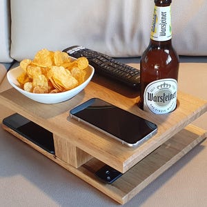 Könnte beinhalten: Ein zweistufiges Serviertablett aus Holz. Die obere Ebene enthält eine Schüssel mit Chips, eine Fernbedienung und eine Bierflasche. Die untere Ebene enthält ein Smartphone und eine Fernbedienung. Das Tablett steht auf einem beigen Sofa.