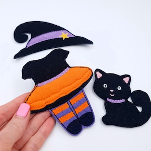 May include: A selection of felt Halloween decorations. Features a black witch's hat with a purple band and gold star, a witch's outfit with orange and purple details, and a black cat with a purple collar.