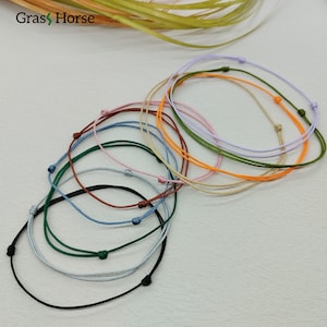 Könnte beinhalten: Eine Sammlung farbiger Schnurarmbänder in verschiedenen Farbtönen, darunter Schwarz, Blau, Grün, Rosa, Orange und Lila. Jedes Armband hat einen einfachen Knotenverschluss. Der Markenname "Gras Horse" ist oben links sichtbar.