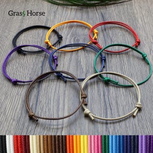 Könnte beinhalten: Eine Sammlung verstellbarer Kordelarmbänder in verschiedenen Farben, darunter Schwarz, Gelb, Rot, Grün, Lila und Braun. Jedes Armband hat einen einfachen Knotenverschluss. Die Abbildung zeigt auch eine Farbpalette der verfügbaren Kordelfarben.