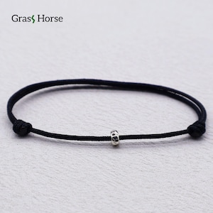 May include: A black cord bracelet featuring a single small, textured silver-toned bead at the center. The bracelet has adjustable knots on both sides. The text Gras Horse is visible in the upper left corner of the image.