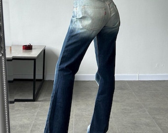 Puede incluir: Vaqueros de mezclilla azul oscuro con una parte superior descolorida y una pierna inferior más oscura. Los jeans tienen un diseño clásico de cinco bolsillos y un parche con el logotipo rojo en la parte posterior. Los jeans se combinan con un top burdeos.