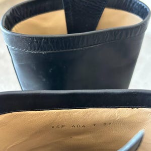 Peut inclure: Gros plan sur une botte en cuir noir. L'int&eacute;rieur est beige avec les chiffres "VSF 404 1 37" imprim&eacute;s sur la semelle int&eacute;rieure. L'ouverture de la botte est visible, r&eacute;v&eacute;lant la doublure int&eacute;rieure et les coutures. La botte est en cuir lisse et brillant.