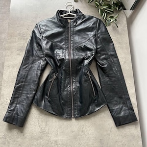 May include: Black leather jacket with a stand-up collar, long sleeves, and a fitted waist. The jacket features a full-length zipper and two zippered pockets. The jacket is hanging on a white hanger.