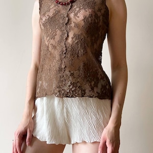 May include: A sleeveless brown lace top with a high collar and a matching red beaded necklace. The top is paired with white pleated shorts. The outfit is displayed on a light background.