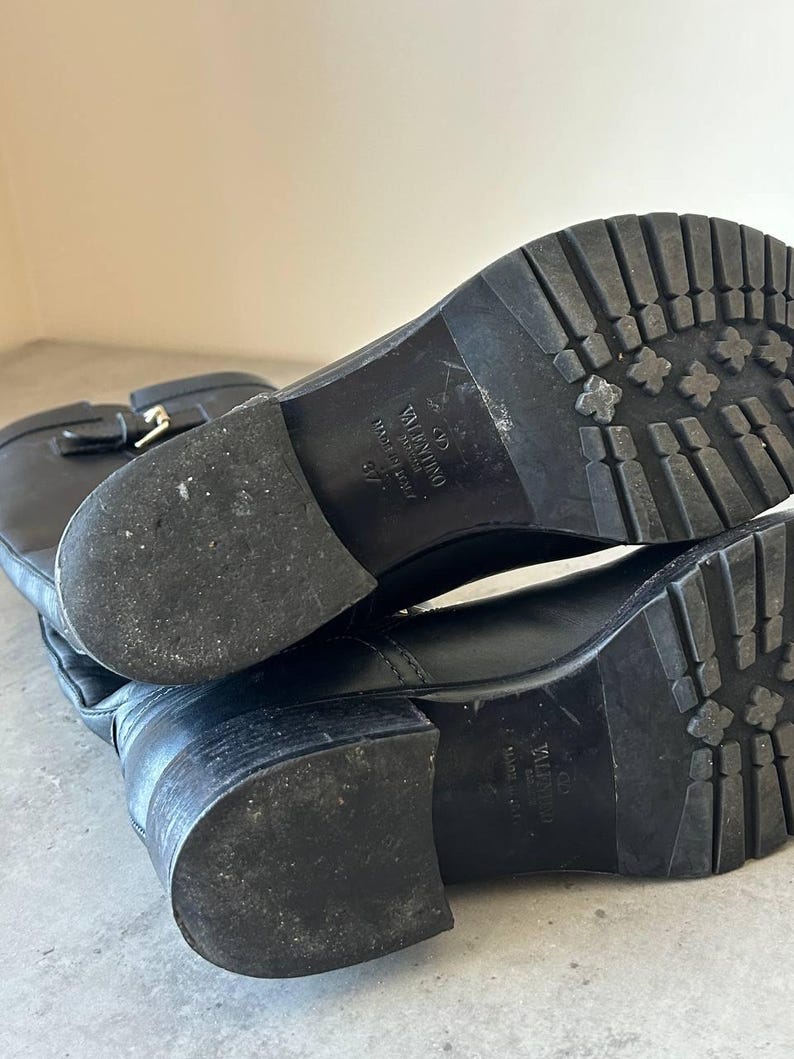 Peut inclure: Bottes en cuir noir avec semelle crant&eacute;e. Les bottes ont une boucle et la marque "Valentino" est visible sur la semelle. Les bottes sont de taille 37.
