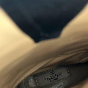 Peut inclure: Vue int&eacute;rieure d'une botte en cuir beige. La semelle int&eacute;rieure porte une &eacute;tiquette rectangulaire avec le logo "Valentino Garavani" en noir. L'int&eacute;rieur de la botte est beige clair, avec une ombre sombre en haut.