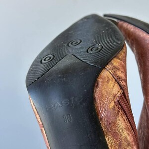 May include: Close-up of the sole of a copper-coloured boot. The black sole has the word "BASIC" and the number "36" printed on it. The boot's upper is a metallic copper colour.