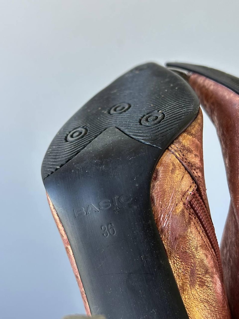 May include: Close-up of the sole of a copper-coloured boot. The black sole has the word "BASIC" and the number "36" printed on it. The boot's upper is a metallic copper colour.