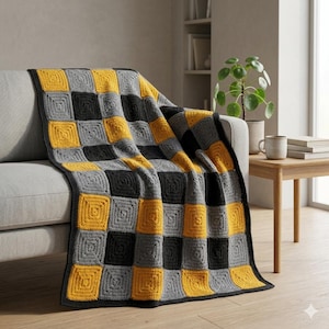 May include: A handmade crochet blanket draped over a gray sofa. The blanket features a checkerboard pattern of yellow, gray, and black squares. The blanket is a cozy home decor item.