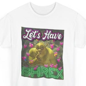Könnte beinhalten: Ein weißes kurzärmeliges T-Shirt mit einem zentralen Aufdruck der Figur Shrek, umgeben von rosa Herzen. Der Text "Let's Have" steht in Weiß über der Figur und das Wort "SHREX" ist in grüner Neon-Schrift unter der Figur abgebildet.