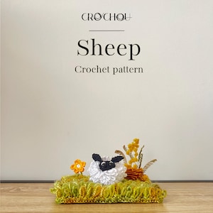 Puede incluir: Una oveja de ganchillo con cara negra y lana blanca, colocada sobre una base de ganchillo verde y amarilla con una pequeña flor naranja y acentos florales amarillos. El texto "Sheep Crochet pattern" está encima de la oveja.