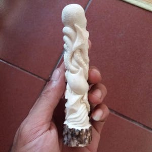 Può includere: Una scultura scolpita color avorio di un polpo. La scultura presenta tentacoli dettagliati e una testa arrotondata. La base della scultura ha un aspetto marrone e strutturato. La scultura è tenuta in una mano.
