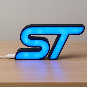 May include: A black and blue illuminated LED sign in the shape of the letters "ST". The letters are outlined in black with a bright blue glow. A white USB cable is connected to the sign, resting on a wooden surface.