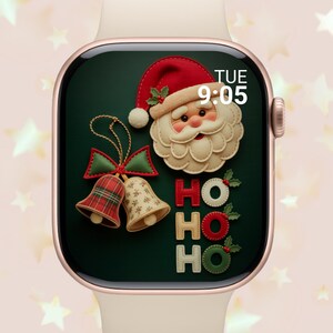 May include: A smartwatch screen displays a festive Christmas design. The face features Santa Claus, bells, and the word "HO" in red and green. The time is 9:05 AM on Tuesday. The watch has a gold case and a light pink band.