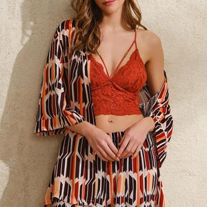 Può includere: Una donna indossa un bralette di pizzo rosso, un kimono fantasia e pantaloni abbinati. Il kimono e i pantaloni presentano un motivo geometrico nei toni del marrone, arancione e bianco. Il bralette ha spalline sottili e scollo a V.