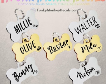 May include: Bone-shaped pet tags in gold and white, each with a pet's name in black script. Some tags feature paw prints, hearts, or other small graphics. The tags are attached to silver rings.