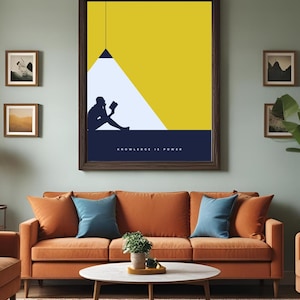 Peut inclure: Une affiche encadrée représentant une silhouette d'une personne lisant sous une lumière, sur un fond jaune et bleu. Le texte « KNOWLEDGE IS POWER » est en bas. L'affiche est au-dessus d'un canapé orange avec des coussins bleus.