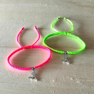 Puede incluir: Dos pulseras de amistad de color neón. Una es rosa brillante, la otra verde neón. Cada pulsera tiene un diseño tejido y un dije plateado de una figura corriendo. Las pulseras son ajustables.