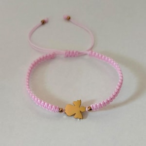 Puede incluir: Una pulsera de macram&eacute; rosa con un dije de &aacute;ngel dorado. La pulsera tiene un cierre de nudo corredizo ajustable. El dije de &aacute;ngel est&aacute; centrado en la pulsera y es una silueta s&oacute;lida y detallada.
