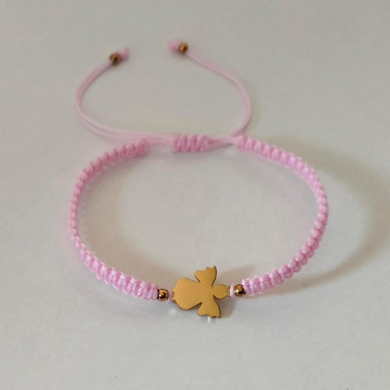 Puede incluir: Una pulsera de macram&eacute; rosa con un dije de &aacute;ngel dorado. La pulsera tiene un cierre de nudo corredizo ajustable. El dije de &aacute;ngel est&aacute; centrado en la pulsera y es una silueta s&oacute;lida y detallada.