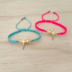 Puede incluir: Dos pulseras hechas a mano. Una es azul claro, la otra rosa intenso. Cada pulsera presenta un dije en forma de estrella de color dorado. Las pulseras están hechas de cordón tejido y tienen cierres ajustables.