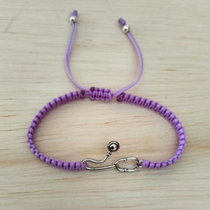 以下が含まれることがあります： 銀色の聴診器チャームが付いた紫色のマクラメブレスレット。ブレスレットはスライドノットで調節可能で、織り込まれたデザインが特徴です。聴診器チャームは、アクセサリーに医療をテーマにしたものを加えています。