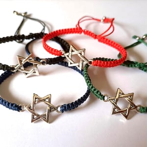 Könnte beinhalten: Vier geflochtene Armbänder mit silbernen Davidstern-Anhängern. Die Armbänder sind rot, dunkelblau, grün und schwarz.