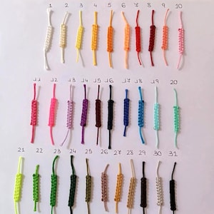 Puede incluir: Una colecci&oacute;n de 31 pulseras de macram&eacute; de colores variados, incluyendo blanco, amarillo, naranja, rojo, rosa, morado, verde y marr&oacute;n. Cada pulsera presenta un dise&ntilde;o anudado y un lazo para sujetar.