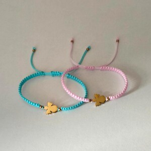 Puede incluir: Dos pulseras de la amistad. Una es azul claro, la otra rosa. Cada pulsera presenta un dije dorado con forma de p&aacute;jaro. Las pulseras son ajustables con un cierre de nudo corredizo. El fondo es de color claro s&oacute;lido.