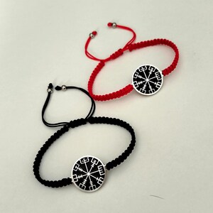 May include: Two adjustable bracelets with black and red string. Each bracelet features a silver charm with a black and white compass design.