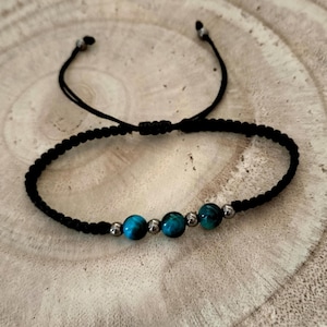 Può includere: Un bracciale in cordino nero con tre perline rotonde color verde acqua vibrante alternate a quattro perline più piccole color argento metallizzato. Il bracciale presenta una fascia in cordino nero intrecciato e due estremità regolabili con piccole perline argentate.